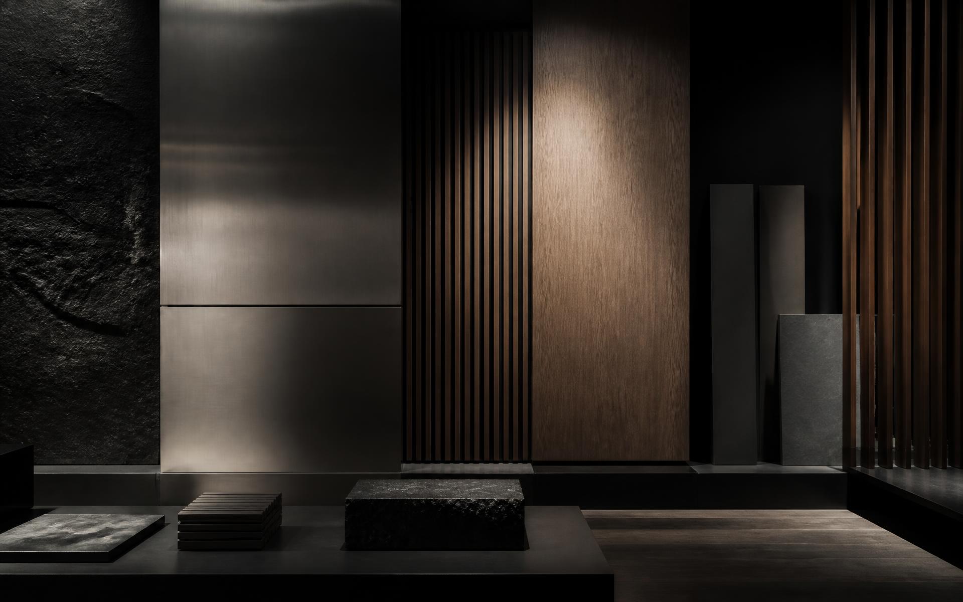 Showroom de matières : panneaux de métal brossé, bois et pierre sous une lumière rasante